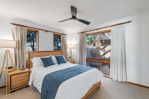 Ein Schlafzimmer mit einem Bett, zwei Nachttischen, einem Deckenventilator und einem großen Fenster mit Vorhängen.