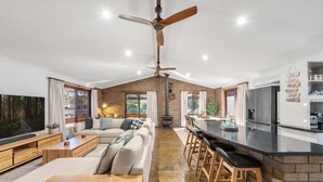 A spacious living area with a sofa set, a dining table with bar stools, a kitchen with a black countertop, and a ceiling fan. - Glassy Waters Sussex Inlet (Sussex Inlet)