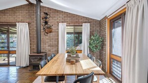 A dining area with a brick wall, a wood-burning stove, a long table, and chairs. - Glassy Waters Sussex Inlet (Sussex Inlet)