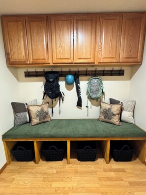 Una habitación con armarios de madera, un banco con cestas de almacenamiento y un soporte en la pared con bolsos y un casco.
