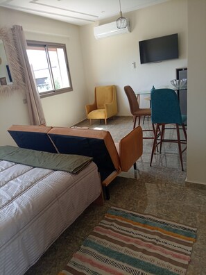 Habitación de hotel con cama, dos sillones, una mesita, televisor y aire acondicionado.