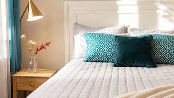 A neatly made bed with a white quilt, a teal patterned pillow, and a dark green pillow.