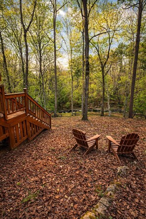 A wooden deck with two Adirondack chairs and a staircase leading into a forest.