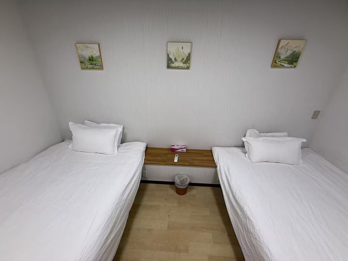 A room with two single beds, a wooden nightstand, and three framed pictures on the wall.