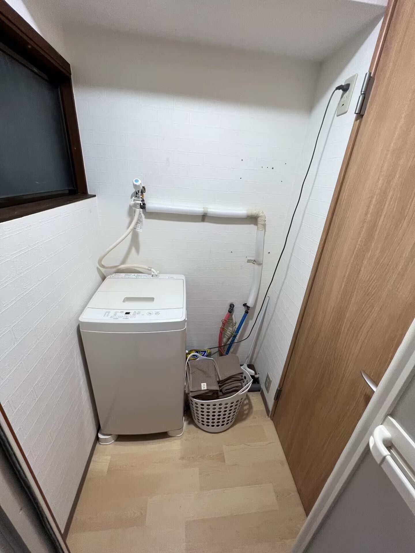 A laundry area with a washing machine, a basket, and a pipe running along the wall.