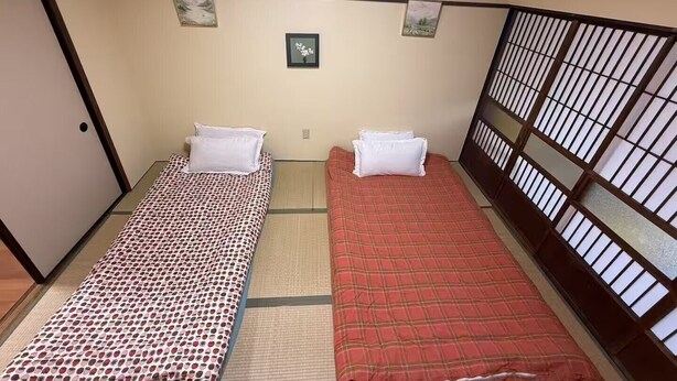 A room with two beds, a tatami mat floor, a wooden door, and a window with a grid pattern. - GORO HOTEL (Tokyo)