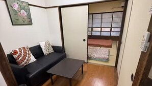 A compact room with a sofa, a small table, a trash bin, and a sliding door leading to a bed area. - GORO HOTEL (Tokyo)