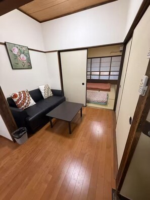 A compact room with a sofa, a small table, a trash bin, and a sliding door leading to a bed area. - GORO HOTEL (Tokyo)