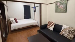A compact room with a bed, a sofa, a coffee table, and a painting on the wall. - GORO HOTEL (Tokyo)