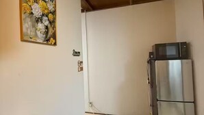 A dining area with a table, chairs, a kettle, a refrigerator, and a painting on the wall. - GORO HOTEL (Tokyo)