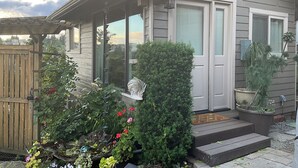 Een huis met een overdekte veranda, een kleine tuin met verschillende planten en bloemen, en een zichtbaar raam.