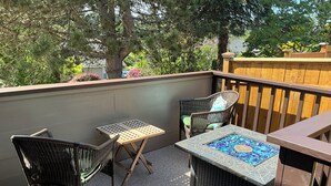 Een balkon met rieten meubels, een mozaiektafel en uitzicht op bomen en een houten schutting.