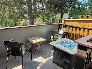 Ein Balkon mit Korbmöbeln, einem Mosaiktablett und Blick auf Bäume sowie einen Holzzaun.