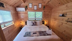 A cozy wooden cabin bedroom with a bed, two bedside tables, a window with blinds, and framed pictures on the wall. - Family Cabin w/ Loft | Arcade | Pigeon Forge (Pigeon Forge)