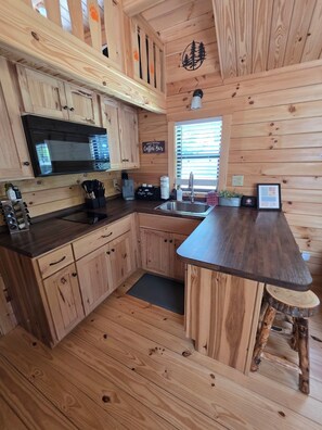 Una cocina de estilo cabaña de madera con microondas integrado, letrero de barra de café y un lavamanos.