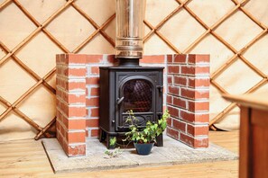 A wood-burning stove with a chimney, surrounded by brick walls and a lattice pattern. - Yurt Sleeps 2 - Bbq & Fire Pit - Dogs Welcome (Bodmin)