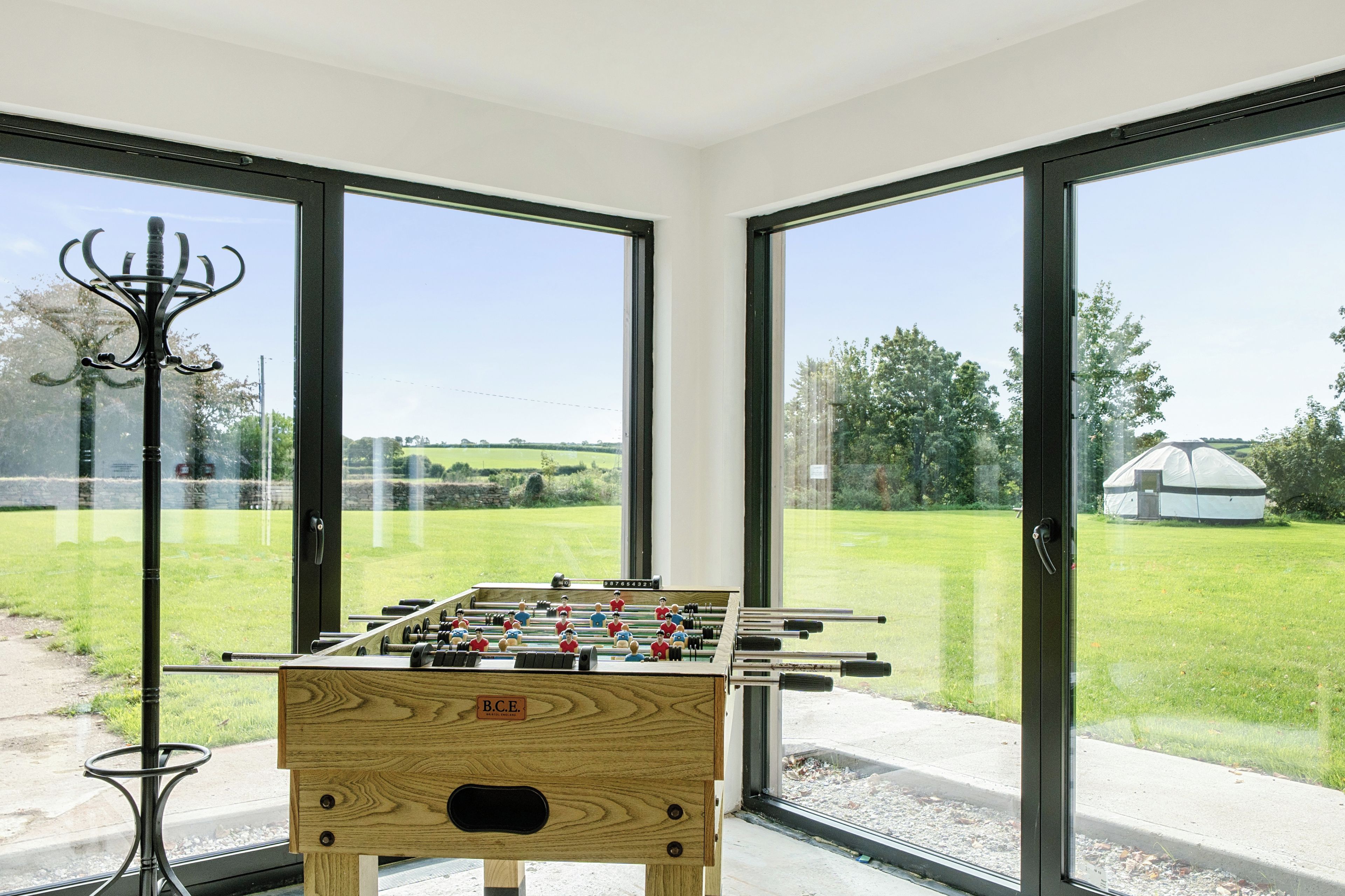 A foosball table in a room with large glass doors leading to a grassy outdoor area.