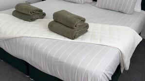 A neatly made bed with white bedding and green towels, a dark green headboard, and a small bedside table with a lamp. - Ayr 2-Bed House, Sleeps 4 with Garden & Parking (Ayr)