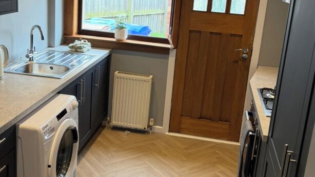 A compact kitchen with a washing machine, a sink, a window, and a door. - Ayr 2-Bed House, Sleeps 4 with Garden & Parking (Ayr)