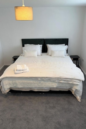 Una cama bien hecha con sábanas y almohadas blancas, un cabecero oscuro y una lámpara colgante.