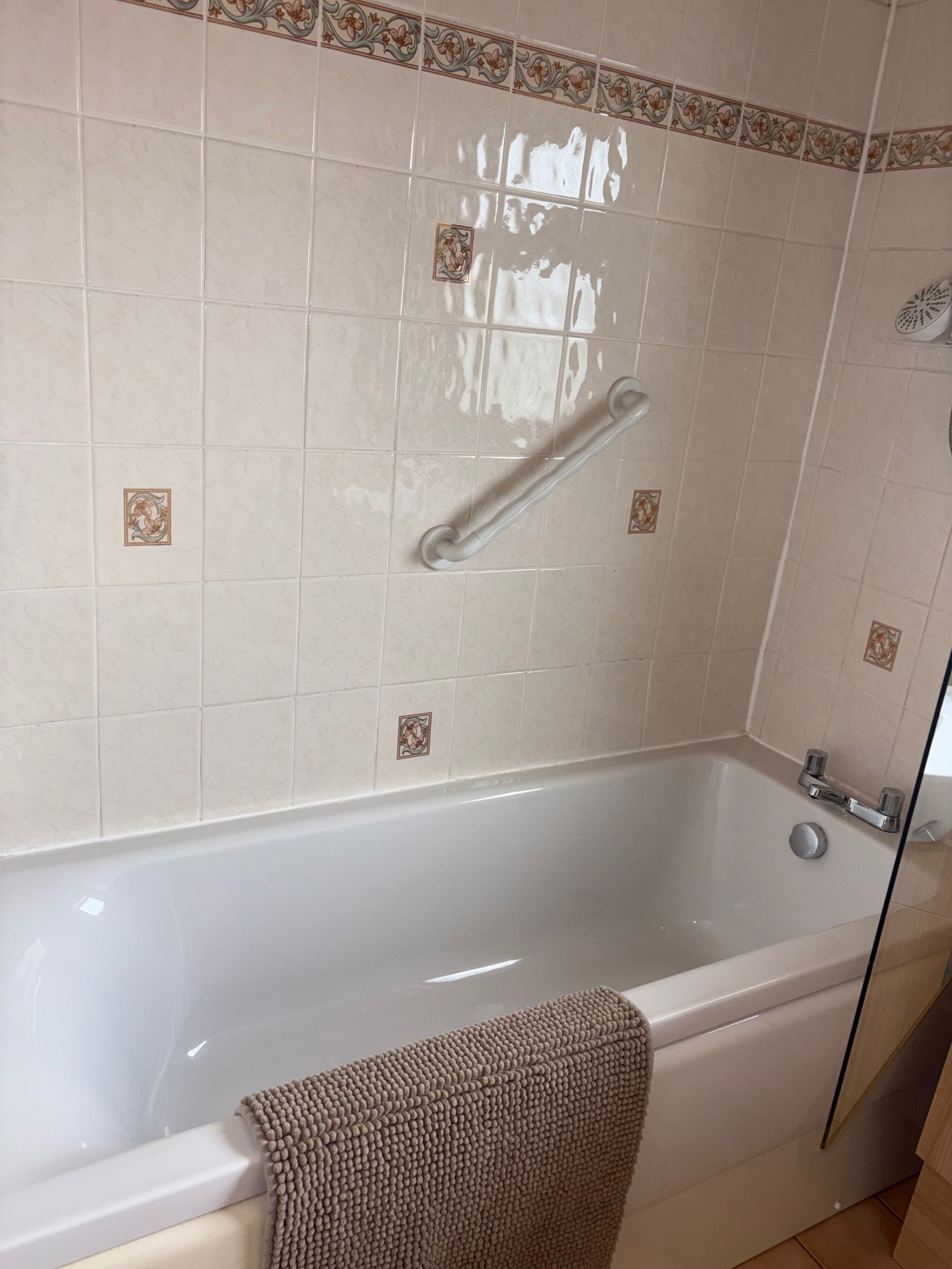 A bathroom with a bathtub, a grab bar, and decorative tiles.