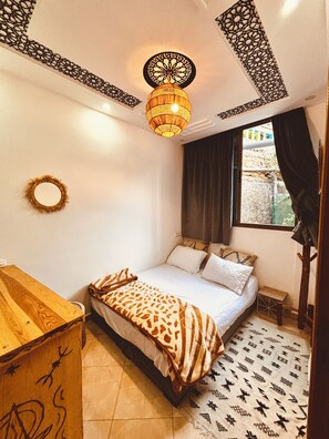 A bedroom with a bed, a wooden dresser, a patterned rug, a decorative wall hanging, and a window with curtains. - Garden view Double Room• 3Min walk to Banana Beach Tamraght . (Tamraght)