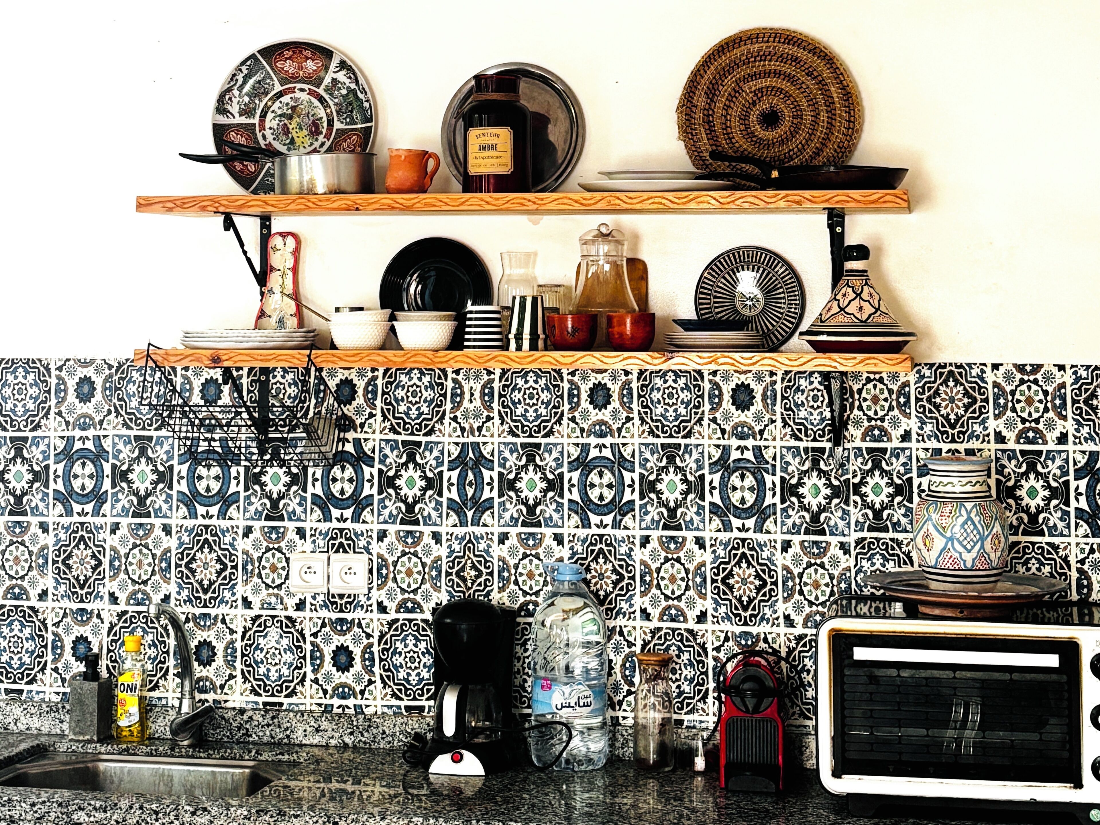 A kitchen with patterned tiles, a coffee maker, a water bottle, and various kitchenware on shelves.