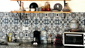 A kitchen with patterned tiles, a coffee maker, a water bottle, and various kitchenware on shelves.