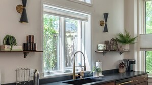 Cocina con armarios de madera, encimera negra, un lavamanos y una ventana con vistas a zonas verdes.