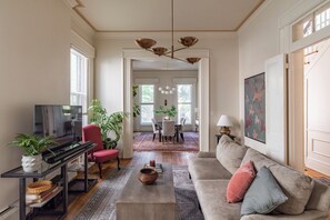 Ein Wohnzimmer mit Fernseher, einer Couch, einem Couchtisch und einem Essbereich mit Stühlen und einem Tisch.