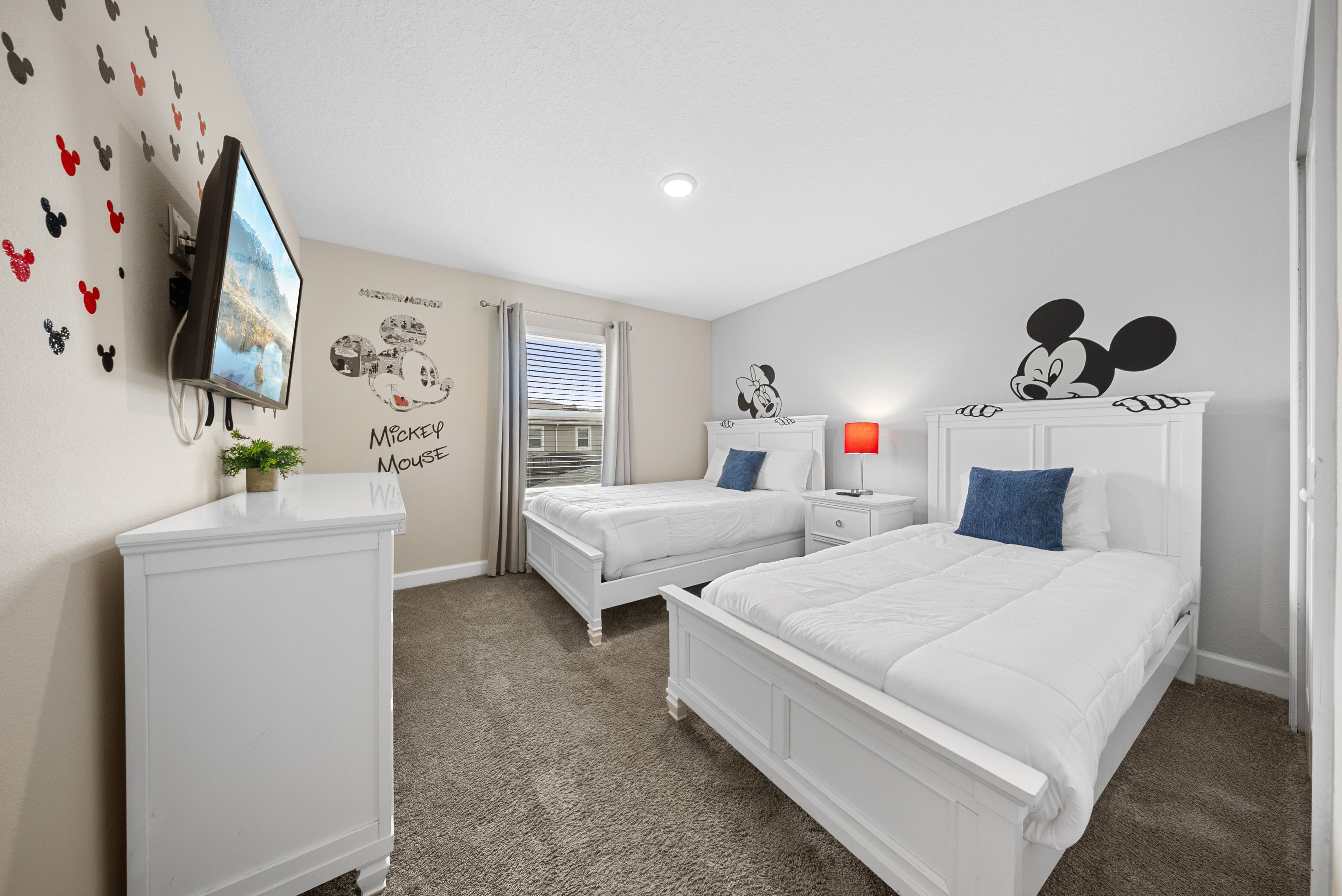 Quarto com duas camas, televisão e adesivos de parede do Mickey Mouse.