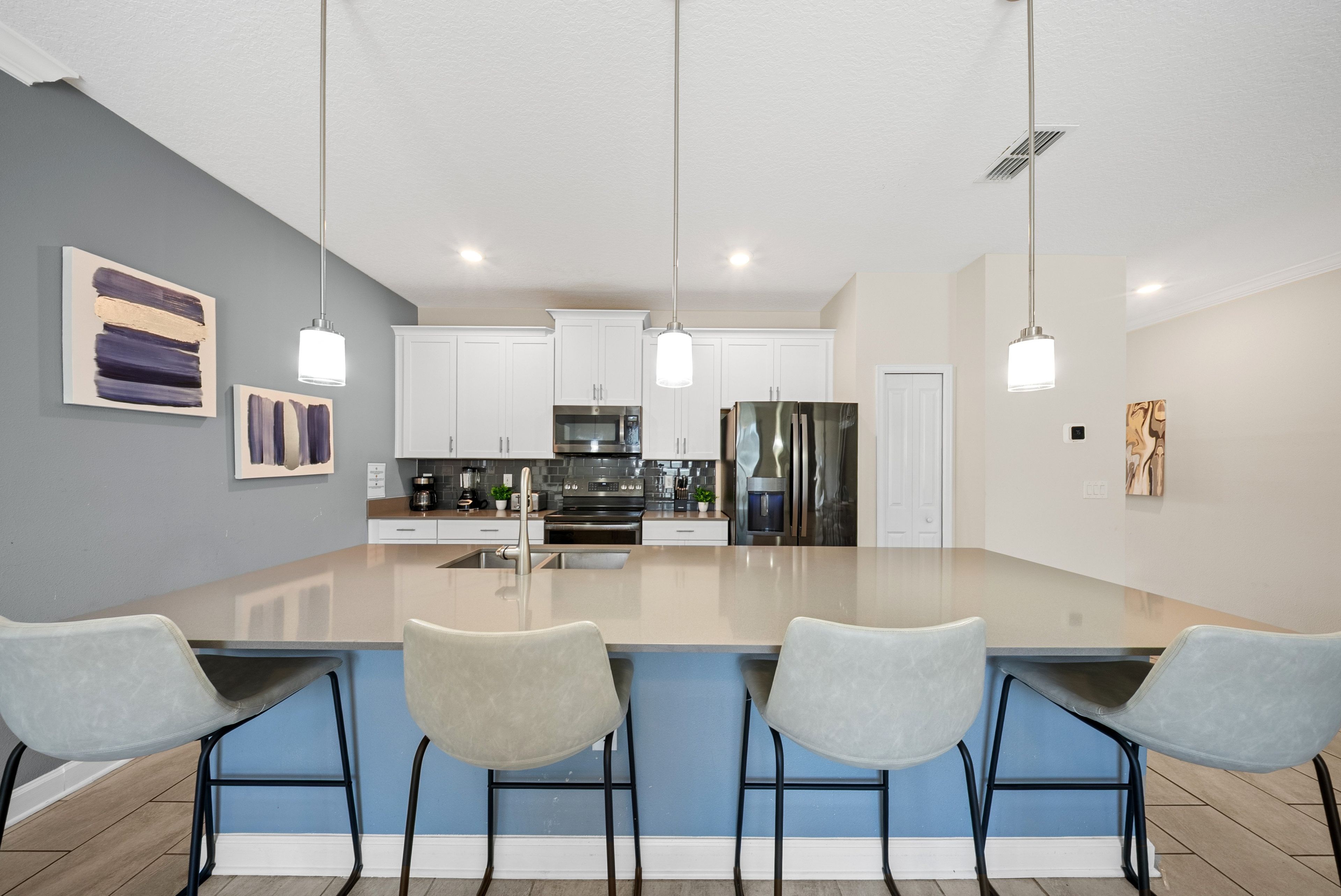 A modern kitchen with a central island, white cabinets, stainless steel appliances, and a blue accent wall.