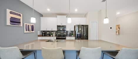 A modern kitchen with a central island, white cabinets, stainless steel appliances, and a blue accent wall.