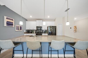 A modern kitchen with a central island, white cabinets, stainless steel appliances, and a blue accent wall. - 2921 SS - Storey Lake Dreamscape (Kissimmee)