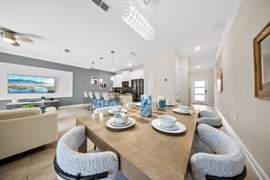 A modern kitchen with white cabinets, a dining area with a wooden table, and a large flat-screen TV mounted on the wall. - 2921 SS - Storey Lake Dreamscape (Kissimmee)