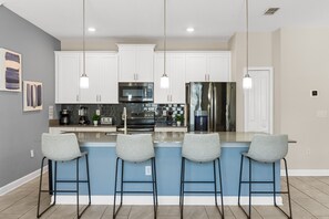 A modern kitchen with a central island, bar stools, stainless steel appliances, and pendant lighting. - 2921 SS - Storey Lake Dreamscape (Kissimmee)
