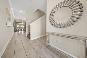 A hallway with a modern staircase, a decorative wall piece, and a dining area in the background. - 2921 SS - Storey Lake Dreamscape (Kissimmee)