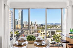A dining area with a city view, a table set with plates and a centerpiece, and a bar area with bottles. - Chevron Renaissance Ocean & River Views (Surfers Paradise)