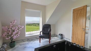 Una habitación con un ventanal grande, un sillón de cuero negro, una puerta de madera y una bañera de hidromasaje negra.