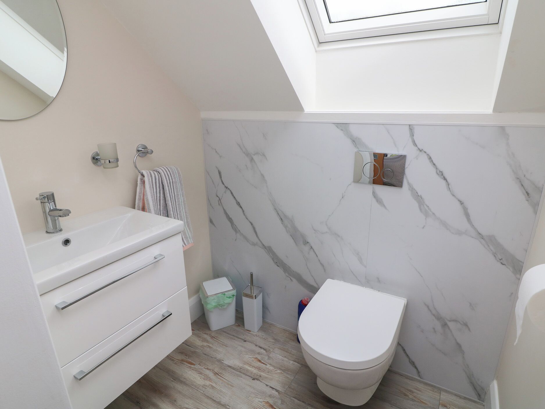A modern bathroom with a white vanity, a toilet, and a marble wall.