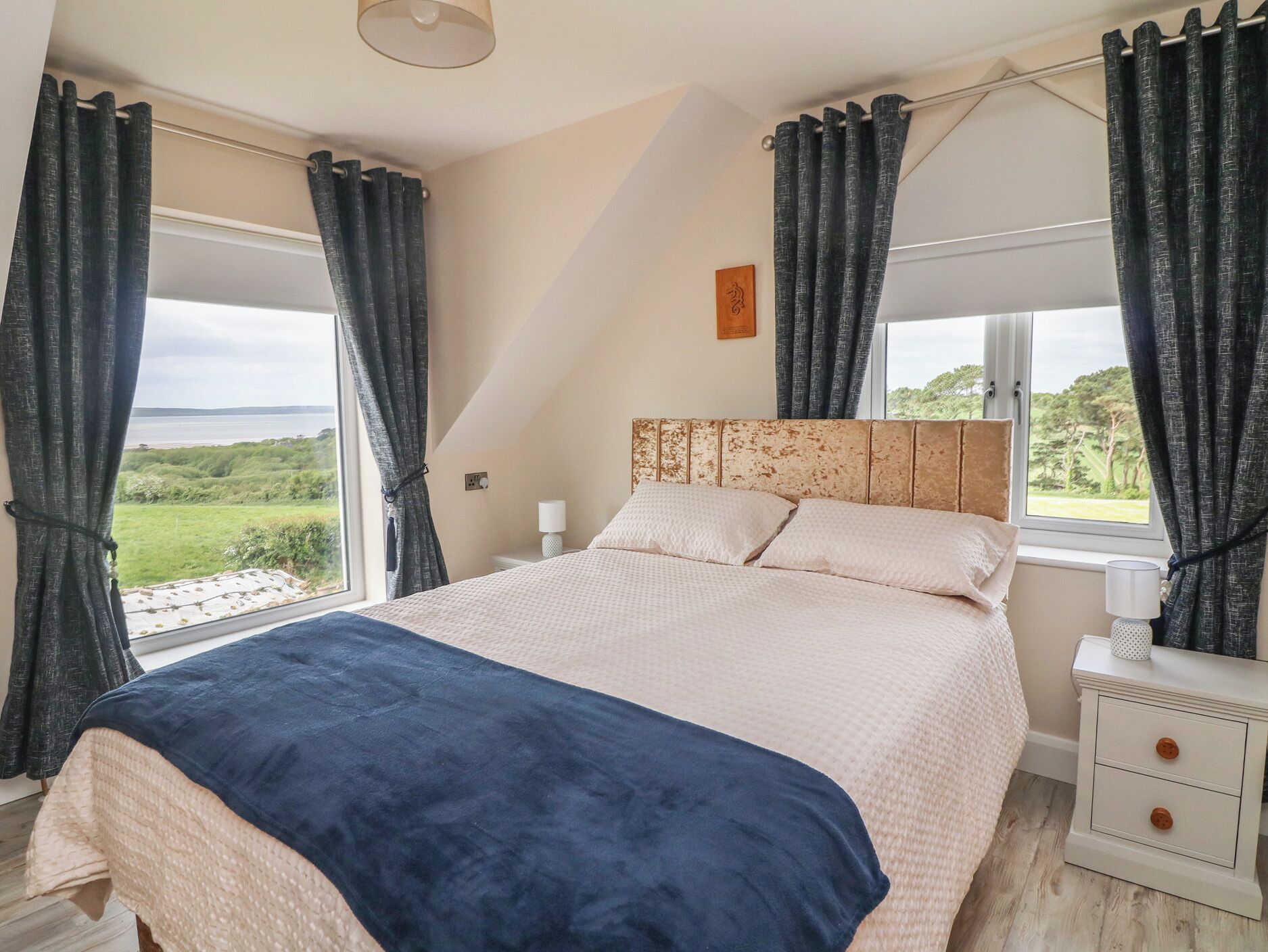 Ein Schlafzimmer mit Bett, Nachttisch, Lampe und Blick ins Freie.
