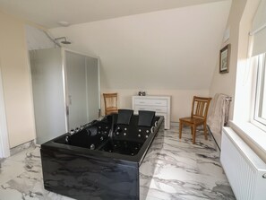 A room with a black jacuzzi, a white cabinet, two wooden chairs, and a radiator.