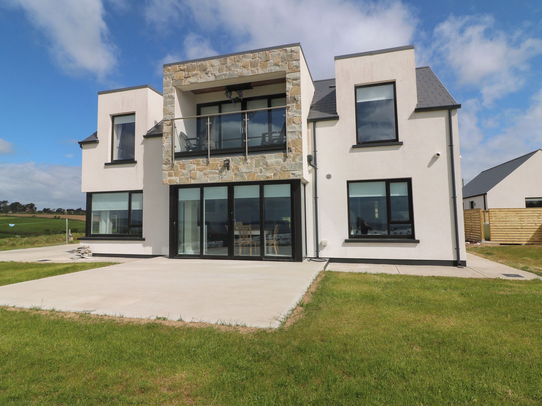A modern two-story house with large windows, a stone facade, and a flat roof.