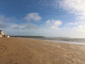 A sandy beach with footprints, a clear sky, and distant hills.