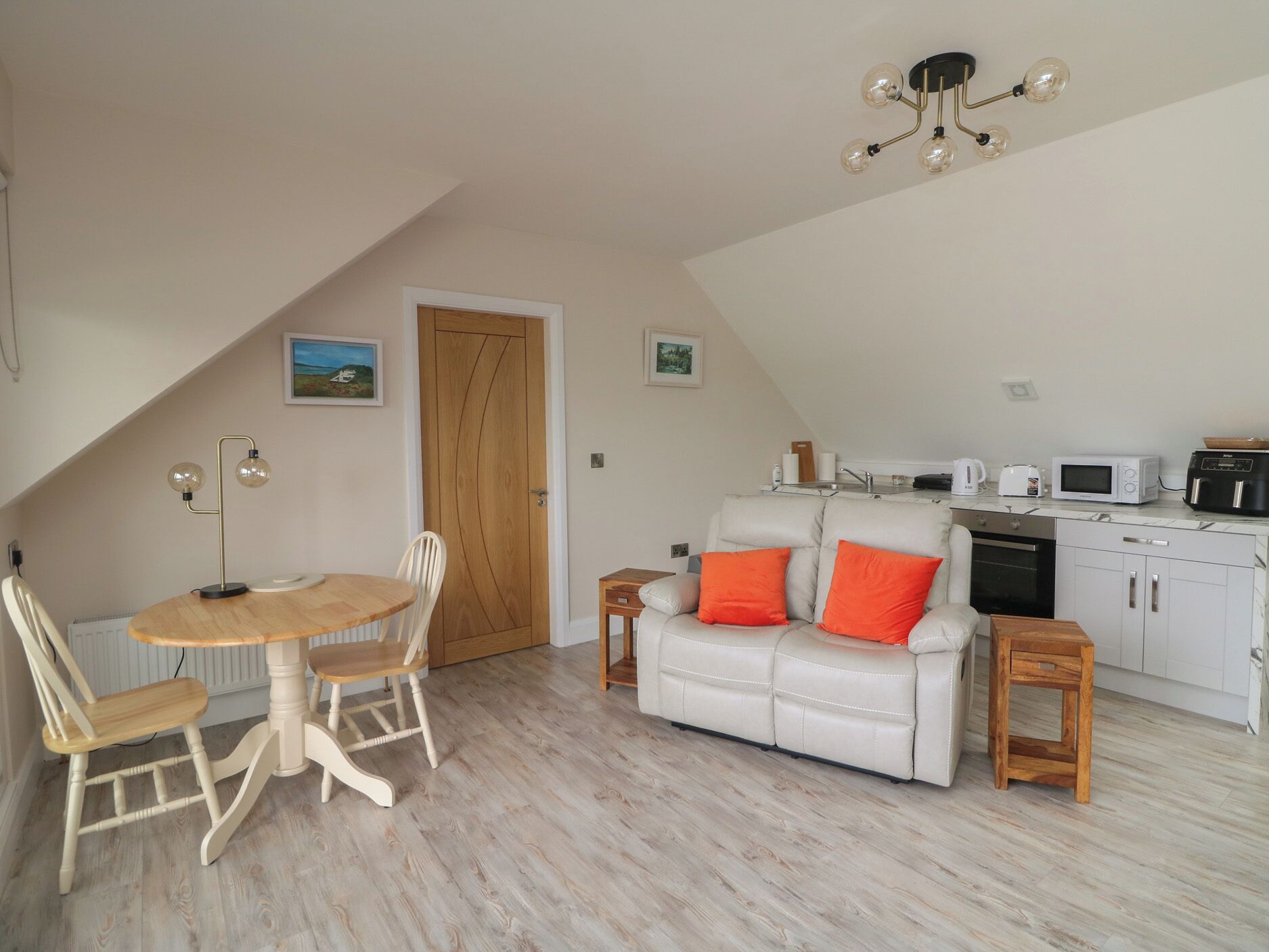 Ein gemütlicher Loft-Raum mit Esstisch, Stühlen, einer Couch mit orangefarbenen Kissen, einer Küchenzeile und einer Deckenleuchte.