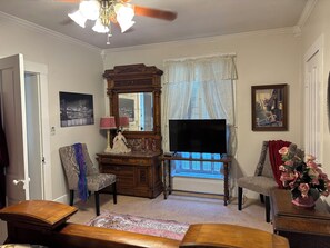 A living room with a television, a wooden cabinet, a chair, a small table, and a window with curtains.