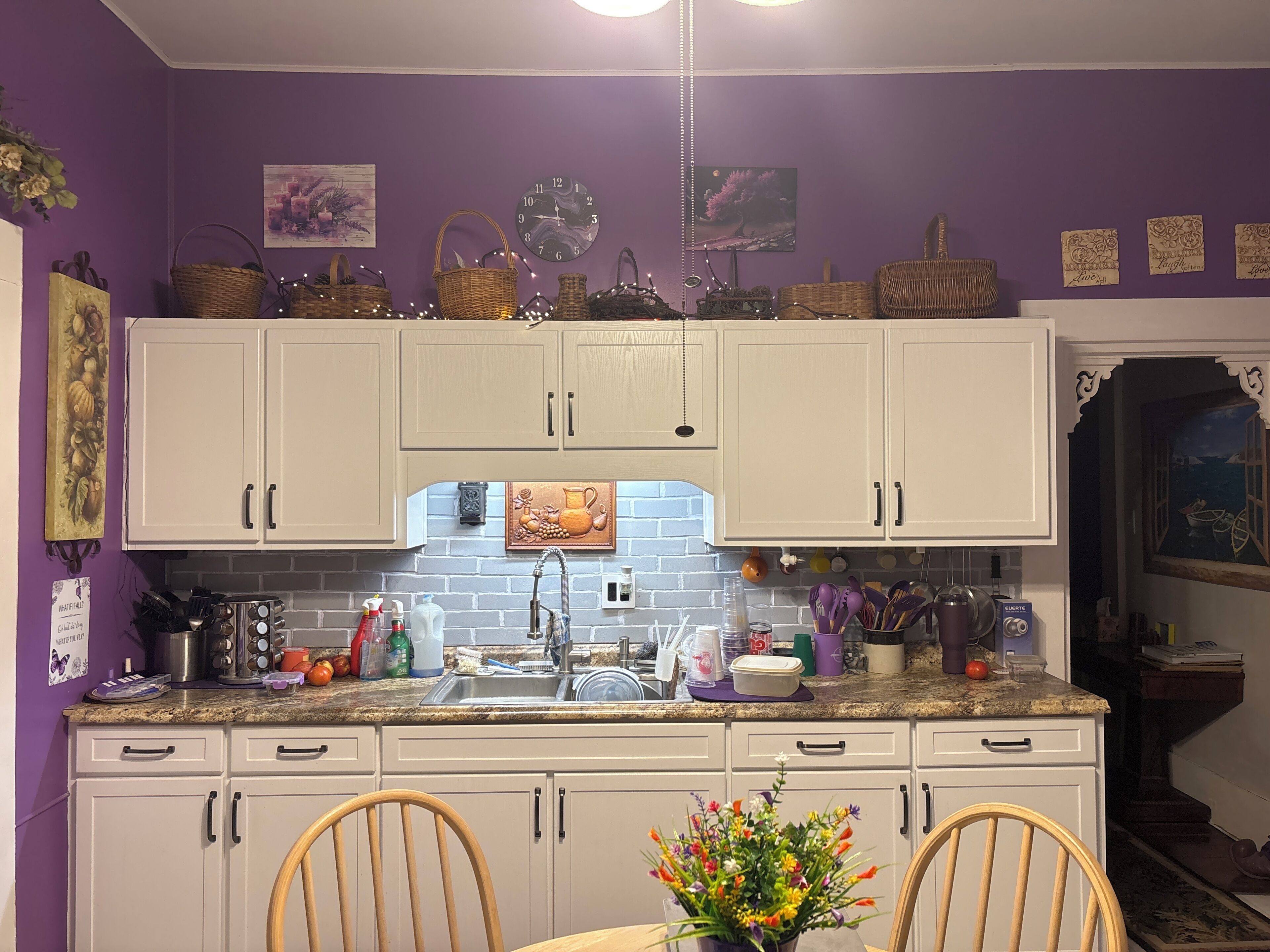 A kitchen with white cabinets, a granite countertop, and a dining area with two chairs.