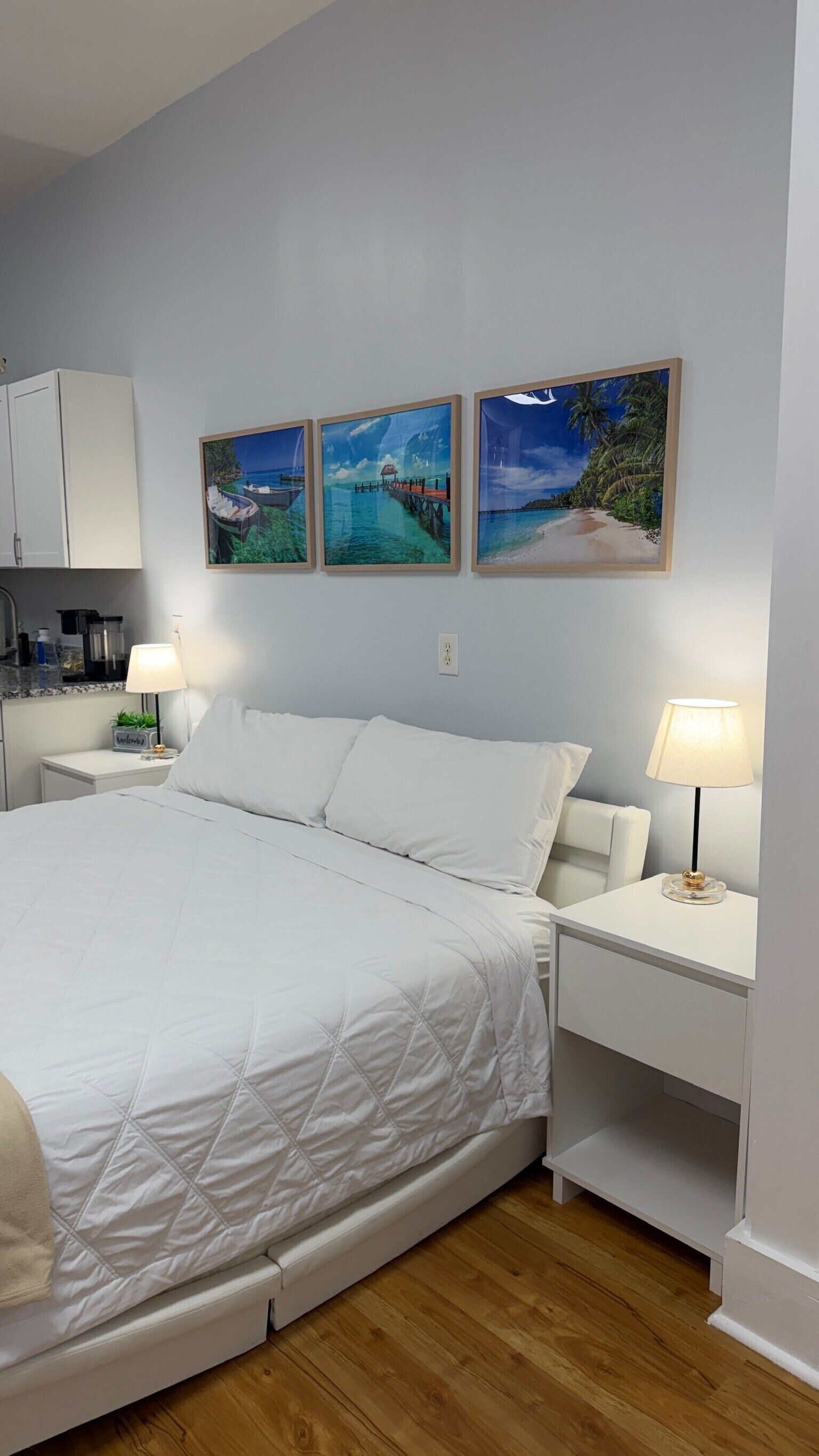 A bedroom with a bed, two bedside tables, a nightstand, a wall-mounted shelf, and three framed pictures.