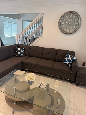 A modern living room with a sectional sofa, a glass coffee table, and a decorative clock on the wall. - The Marble Manor by Boardwalk (Myrtle Beach)