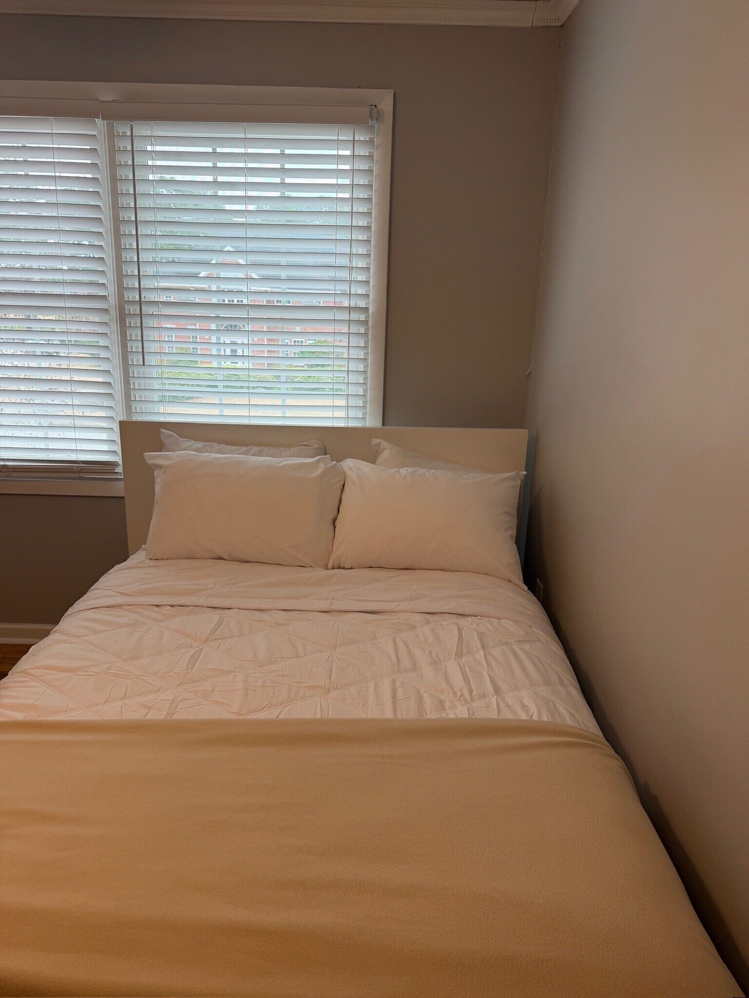 Uma cama de solteiro com roupa de cama branca num quarto com janela e parede lisa.